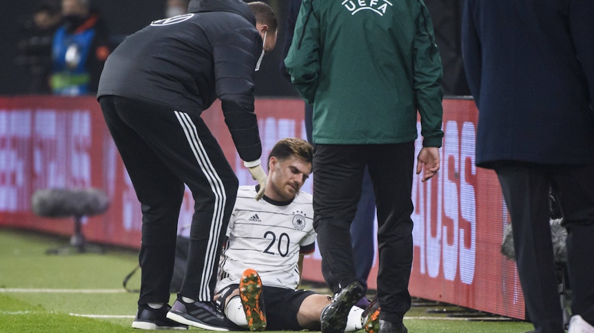 Gladbachs Nationalspieler Jonas Hofmann (M.) sitzt mit einem Muskelbündelriss im rechten Oberschenkel auf dem Rasen der Leipziger Arena und wird von einem Mediziner behandelt.