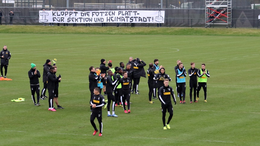Training vorbei, die Borussia-Profis bedanken sich für die Unterstützung. Im Hintergrund ein fragwürdiges Plakat.