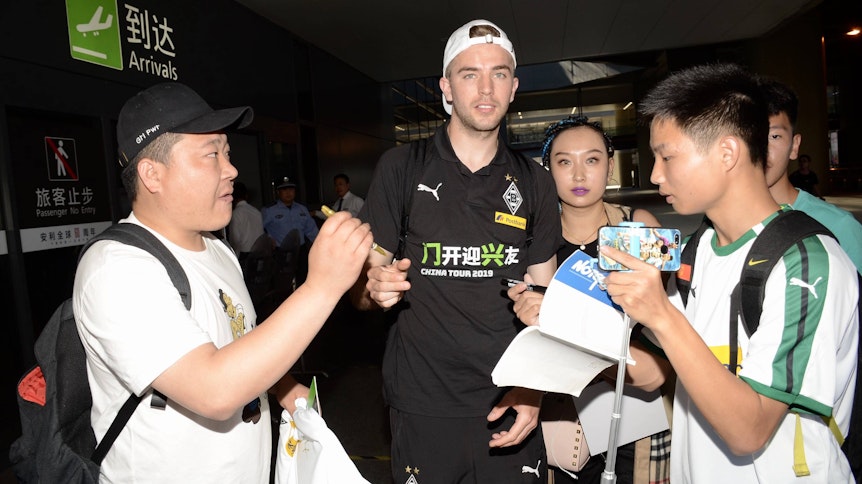 Fußballer Christoph Kramer wird am Flughafen in Shanghai von mehreren Fans umlangert und schreibt Autogramme.