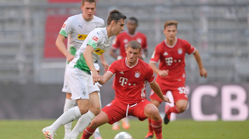 Florian Neuhaus (links) von Borussia Mönchengladbach führt den Ball, Michael Cuisance, im roten Bayern-München-Trikot, möchte ihm diesen abnehmen.