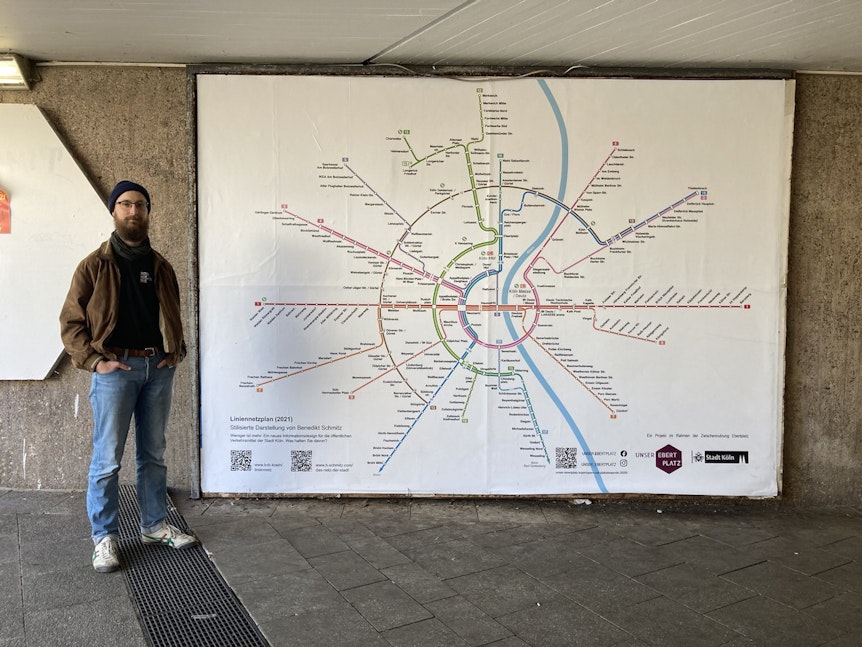Benedikt Schmitz steht neben seinem Liniennetzplan, der als großes Plakat auf dem Ebertplatz ausgestellt wird.