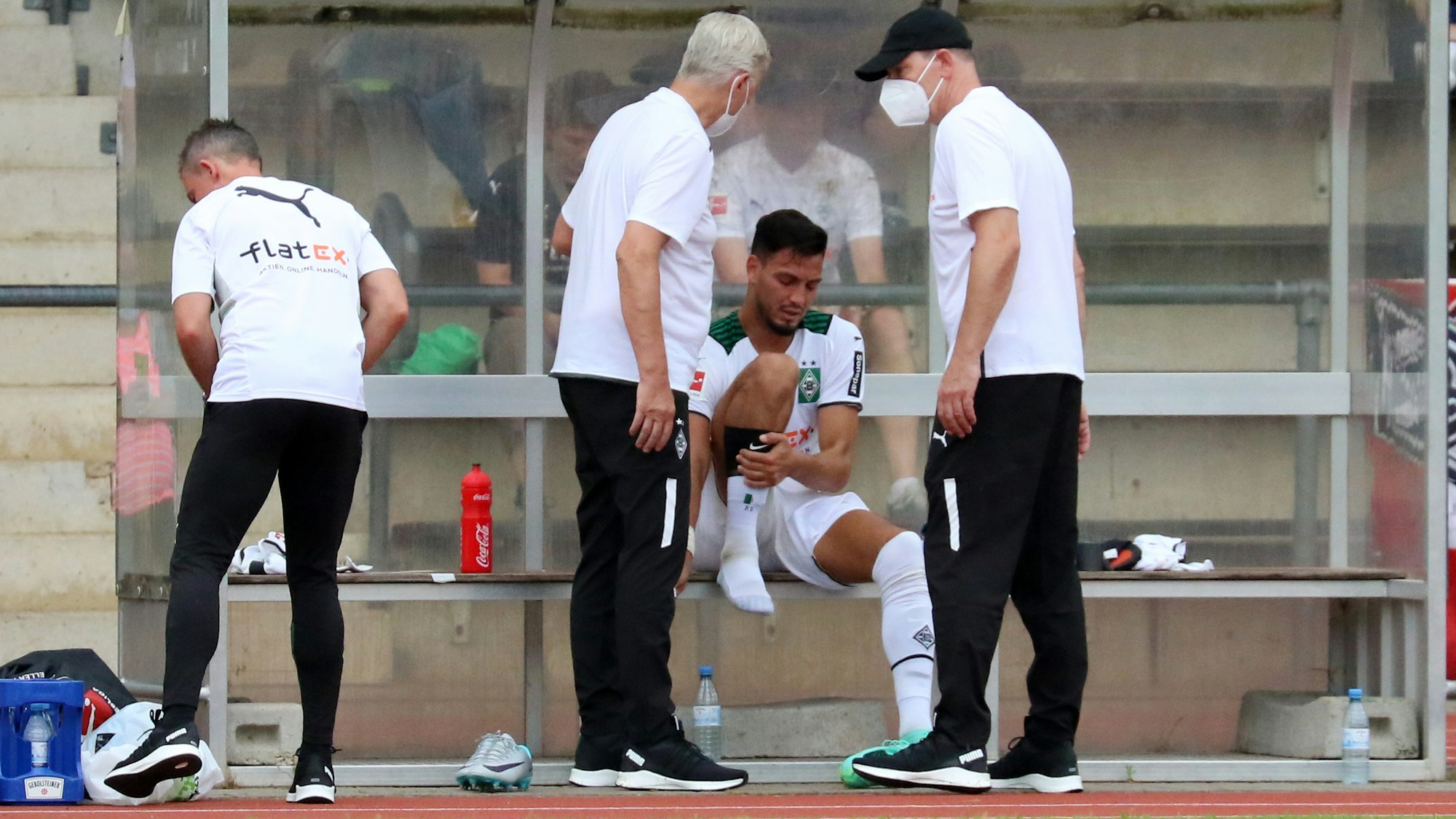 Gladbach-Verteidiger Ramy Bensebaini sitzt auf der Auswechselbank, die Physios schauen sich seinen Fuß beim Testspiel gegen Viktoria Köln am 10. Juli 2021 im Grenzlandstadion an.