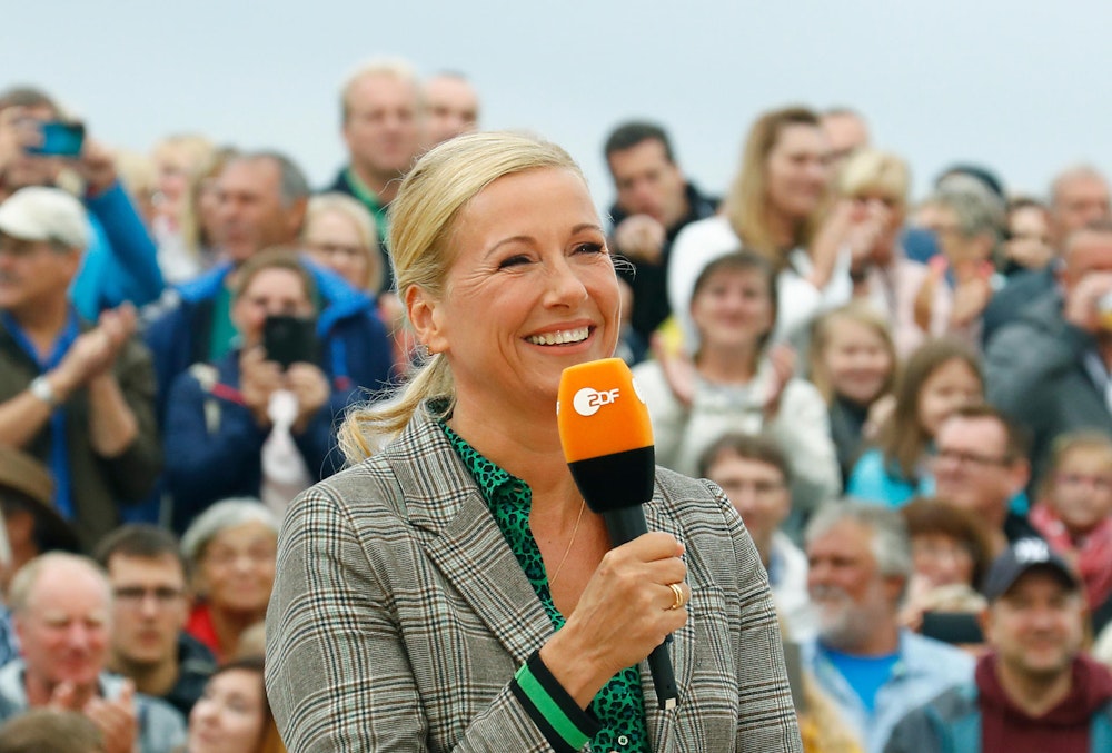 Andrea Kiewel hält im Fernsehgarten ZDF-Mikro in der Hand und lacht.