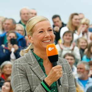 Andrea Kiewel hält im Fernsehgarten ZDF-Mikro in der Hand und lacht.