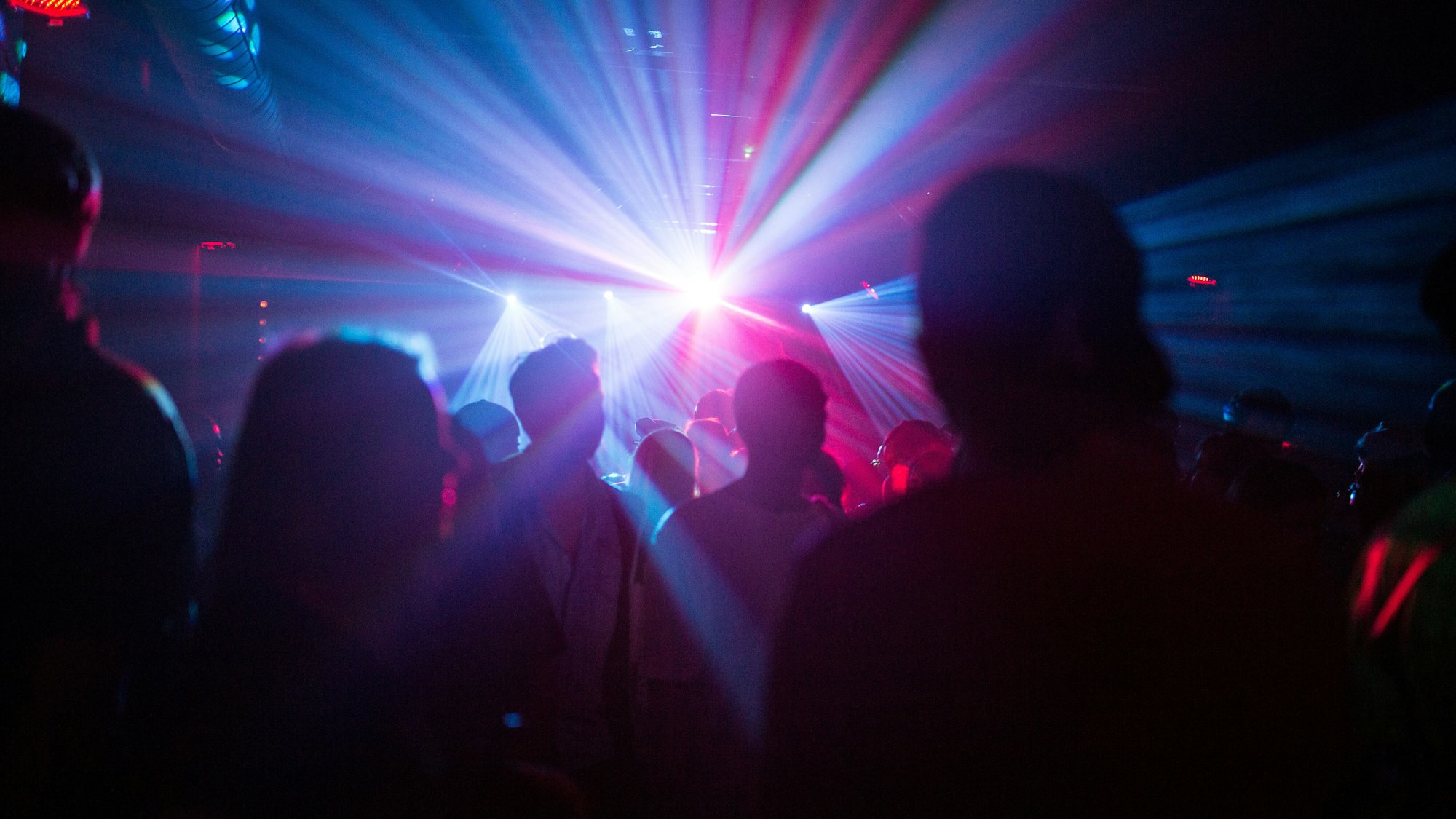 Menschen feiern in dem Symbolbild in einer Disco, Silhouetten sind im Laser-Licht zu sehen.Eine Reiserückkehrerin aus Mallorca sorgte in einem Club in Karlsruhe für einen Corona-Ausbruch.