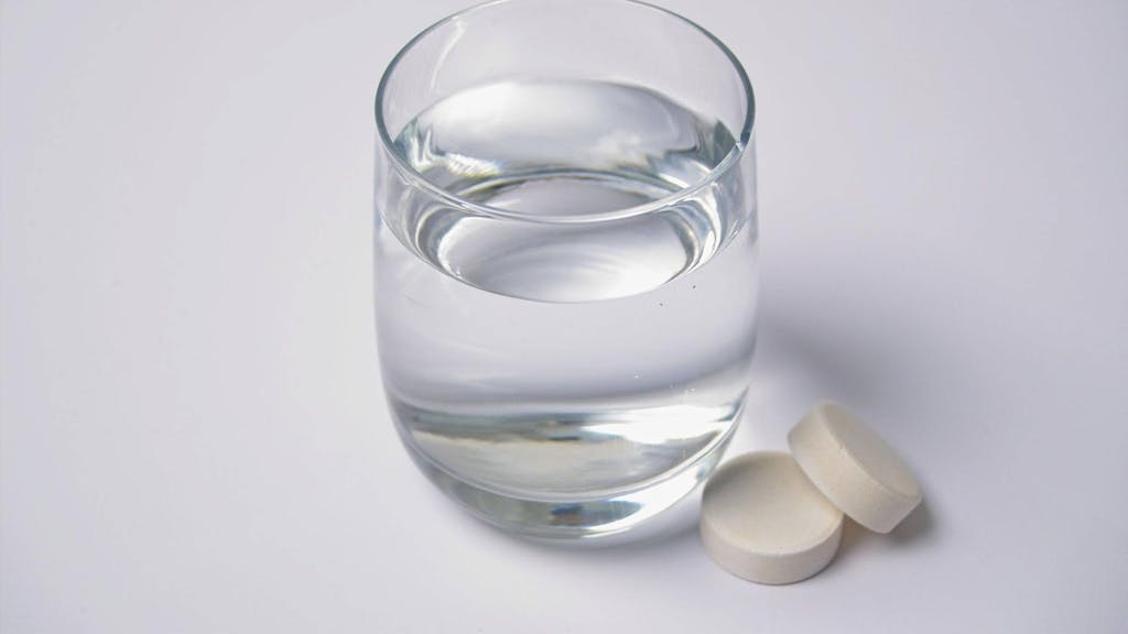 Das Symbolbild zeigt ein Wasserglas mit zwei Tabletten, die daneben liegen.&nbsp;Der Hersteller Abtei ruft bestimmte Vitamin-Präparate zurück, die bundesweit verkauft wurden.