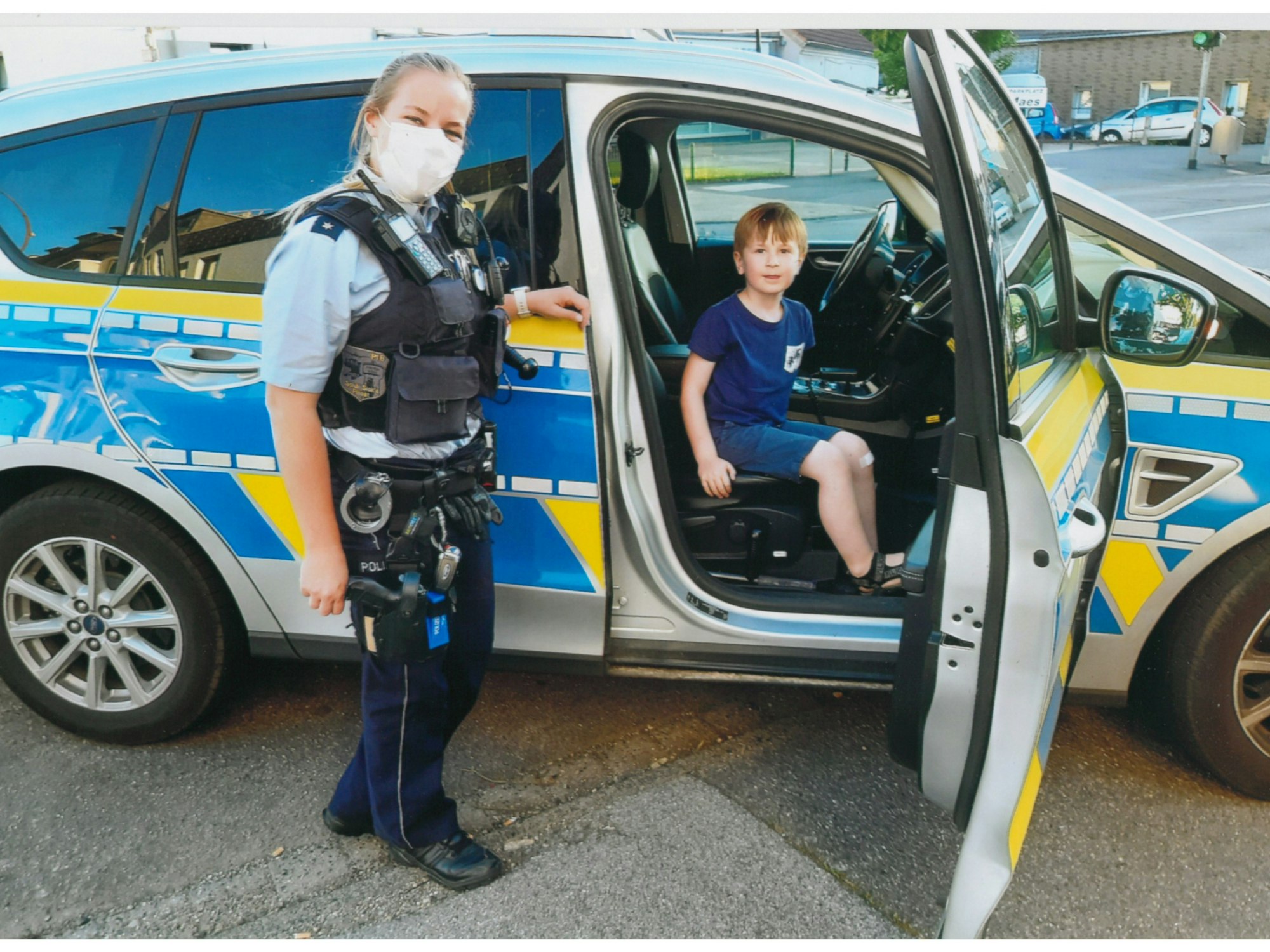 Klaas (5) aus Köln hat auf dem Beifahrersitz des Streifenwagens Platz genommen. Polizistin Lynn steht daneben.
