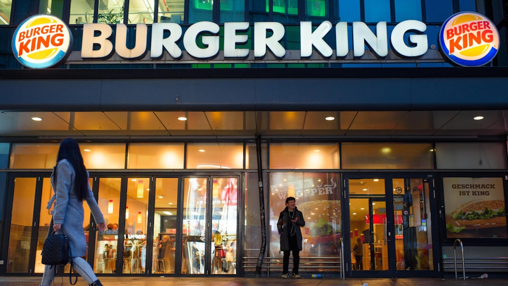 Passanten und Passantinnen gehen am Abend an einer Burger King-Filiale auf dem Alexanderplatz in Berlin vorbei.