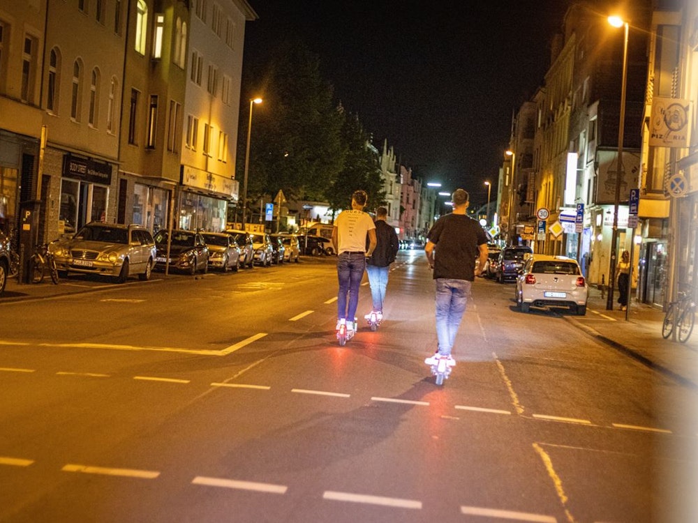 Junge Männer fahren in der Nacht auf E-Scootern auf der Berrenrather Straße in Köln-Sülz.
