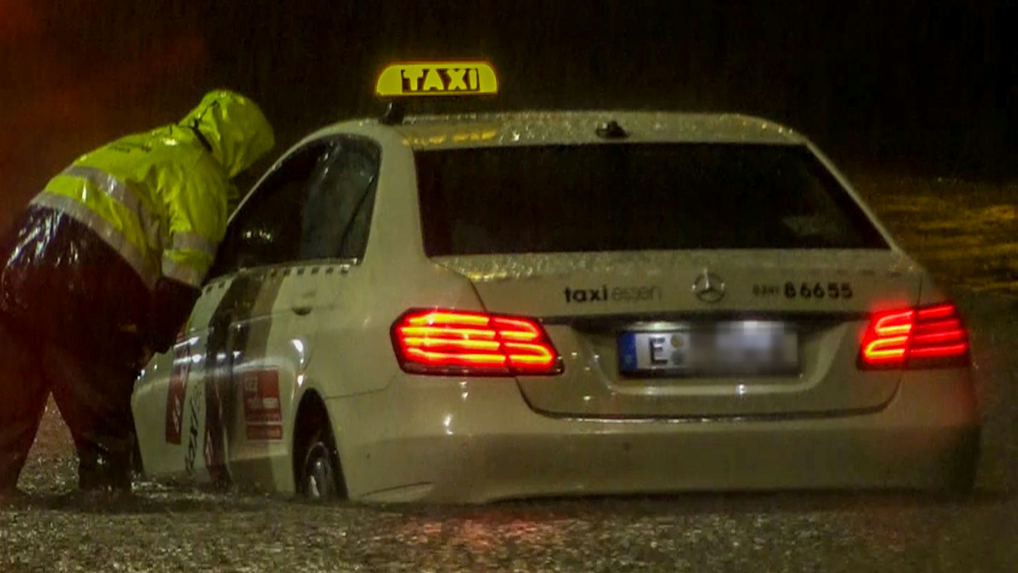Ein Feuerwehrmann spricht mit dem Fahrer eines Taxis, das sich im Hochwasser festgefahren hat. Starkregen lässt Straßen überfluten.