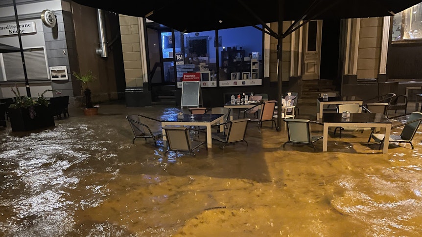 Tische und Stühle sind in Hagen halb von Wasser überflutet, sie stehen vor einem Hauseingang.