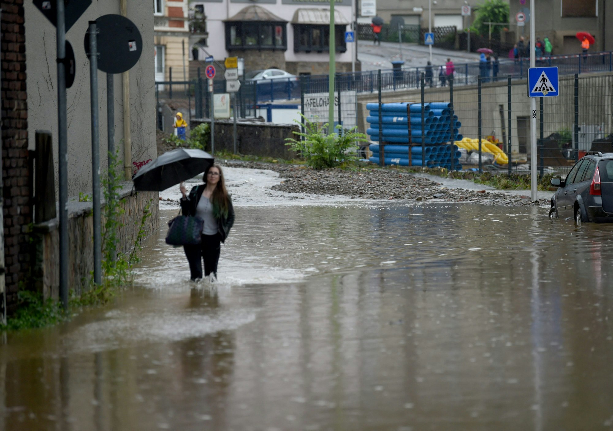 Eine Frau mit einem Regenschirm läuft am 14. Juli 2021 über eine überschwemmte Straße in Hagen.
