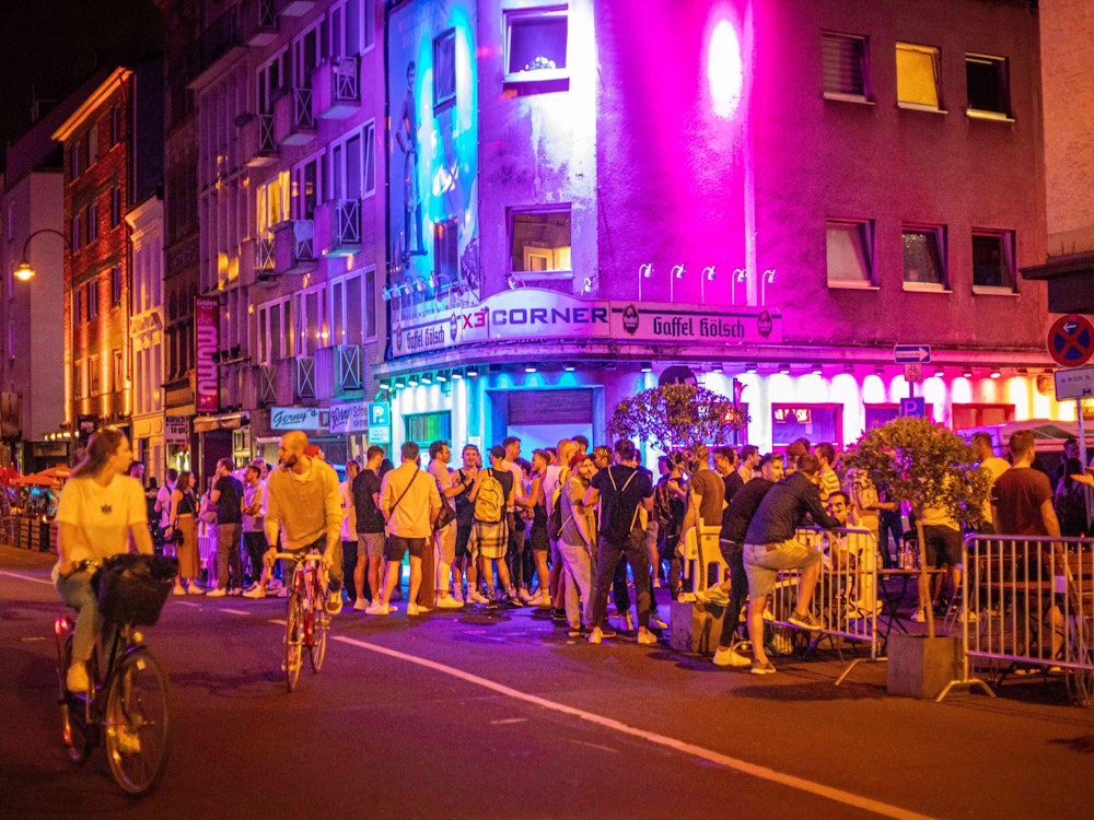 Vor einer Bar an der Schaafenstraße in Köln stehen zahlreiche Party-Gäste.