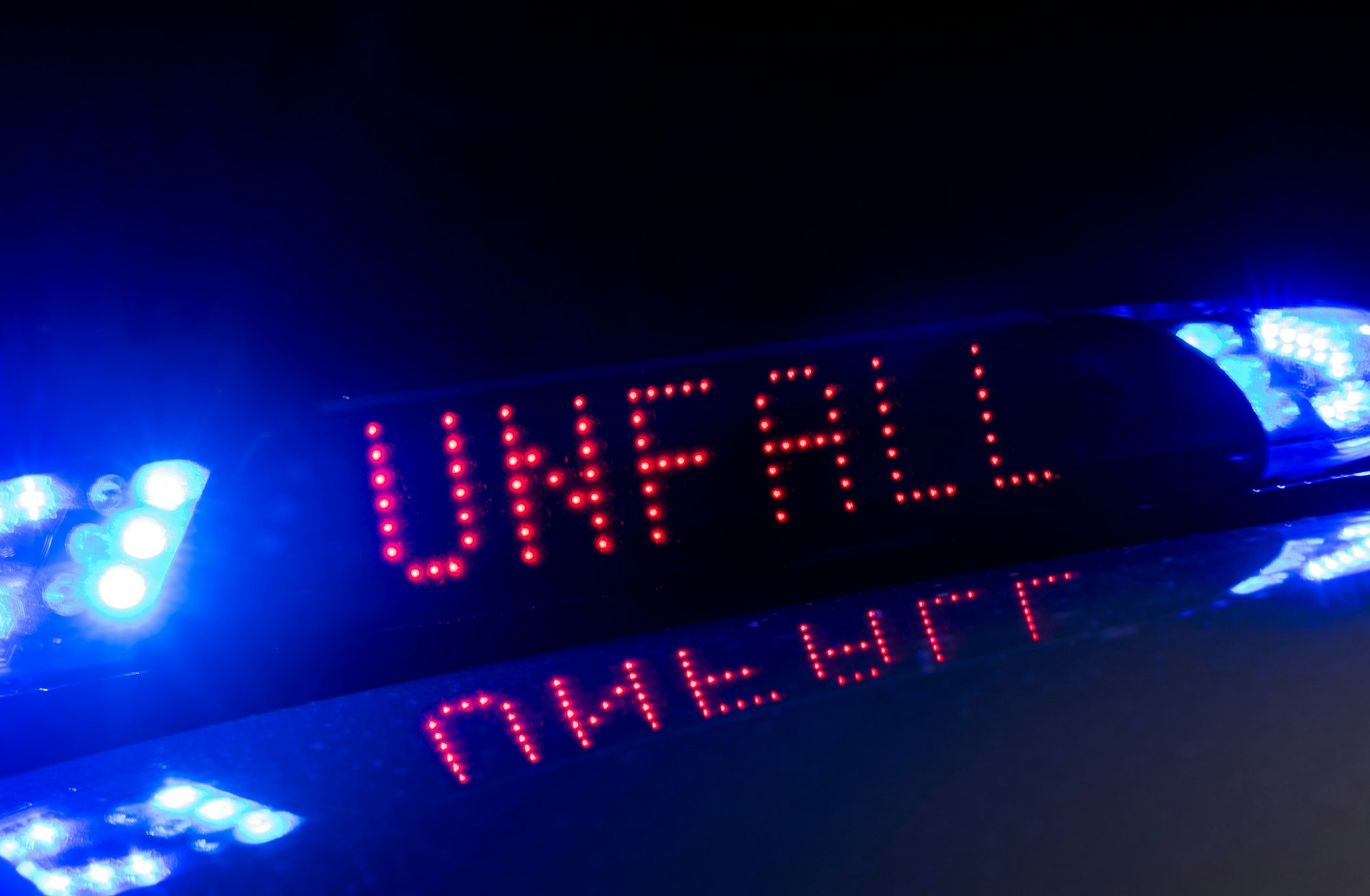 Das Blaulicht auf einem Fahrzeug der Polizei leuchtet in der Dunkelheit, während auf dem Display der Hinweis „Unfall “zu lesen ist.