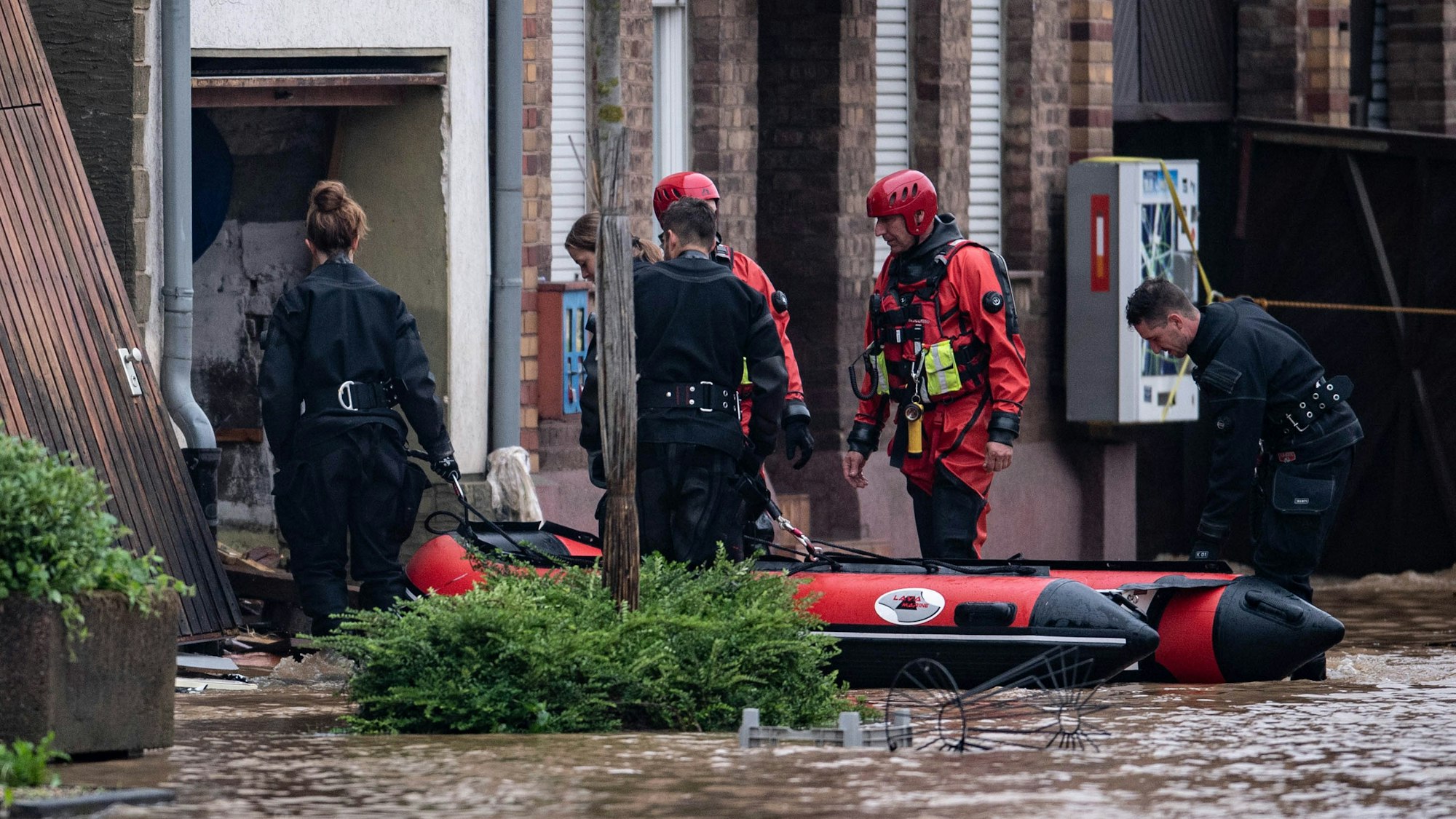 Rettungsschwimmer und Polizeitaucher begeben sich mit einem Schlauchboot in einen überfluteten Innenhof.