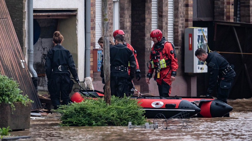 Rettungsschwimmer und Polizeitaucher begeben sich mit einem Schlauchboot in einen überfluteten Innenhof.