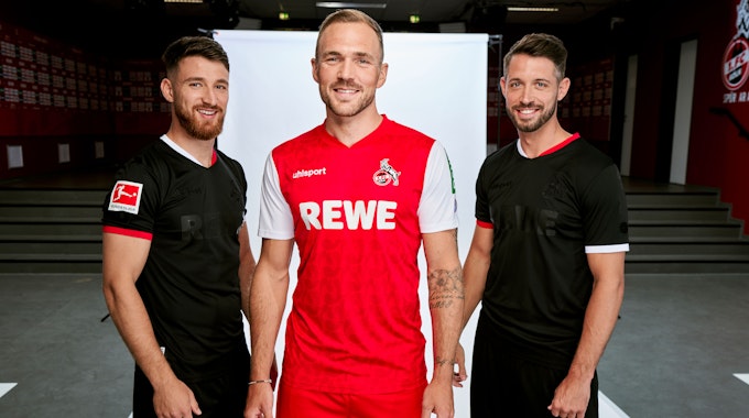 Die Profis Rafael Czichos (M.) sowie Salih Özcan (l.) und Mark Uth präsentieren das neue Auswärtstrikot in Rot und Weiß sowie das schwarze Ausweichdress des 1. FC Köln.