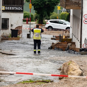 Ein Feuerwehrmann steht auf einer Straße, die zum Königssee führt, und über die noch Wasser abfließt.