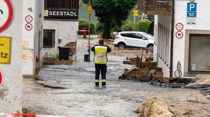 Ein Feuerwehrmann steht auf einer Straße, die zum Königssee führt, und über die noch Wasser abfließt.