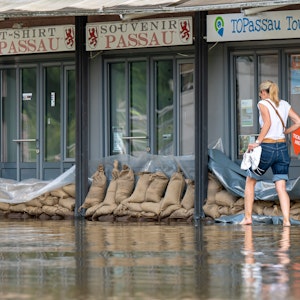 Eine Frau geht in Passau an der Uferpromenade an einem Reise-Center vorbei, das mit Sandsäcke vor den Türen vor dem Wasser der Donau abgedichtet wurde.