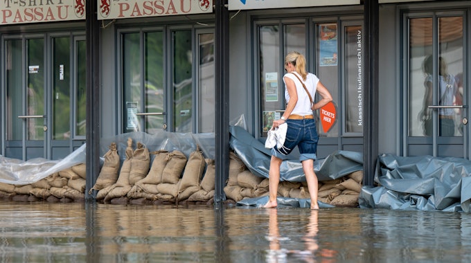 Eine Frau geht in Passau an der Uferpromenade an einem Reise-Center vorbei, das mit Sandsäcke vor den Türen vor dem Wasser der Donau abgedichtet wurde.