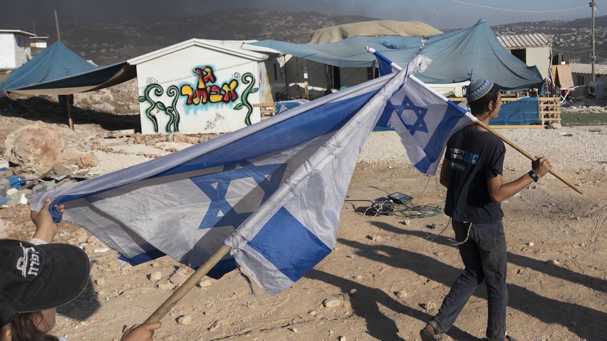 Zwei Menschen schwenken in einer Siedlung Israel-Flaggen im Westjordanland.