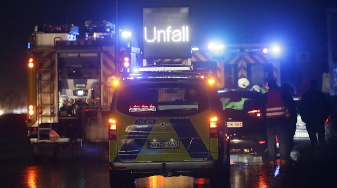 Polizei- und Feuerwehrfahrzeuge mit Blaulicht sichern eine Unfallstelle auf der Autobahn.