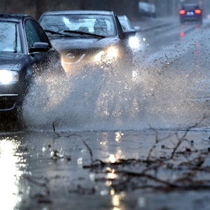 Gelsenkirchen: Autos fahren langsam durch eine tiefe Pfütze die sich durch Starkregen auf einer Straße gebildet hat.