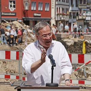 Armin Laschet spricht in ein Mikrofon. Im Hintergrund sieht man die Unwetterschäden in Bad Münstereifel, die mit einem Bauzaun abgesperrt sind.