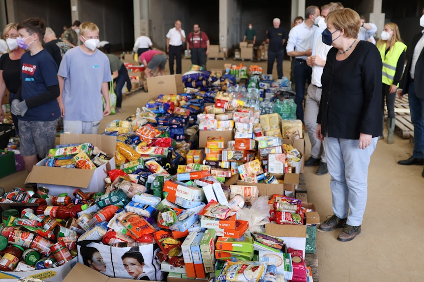 Bundeskanzlerin Angela Merkel (CDU, r)besichtigt ein Lager mit Lebensmitteln bei ihrem Besuch im vom Hochwasser betroffenen Gebiet von Bad Münstereifel.