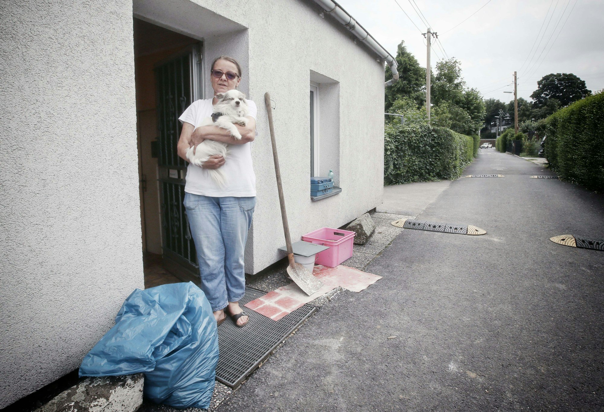 Eine Frau steht mit ihrem Hund vor ihrem Haus, das beim Hochwasser in Düsseldorf beschädigt wurde.
