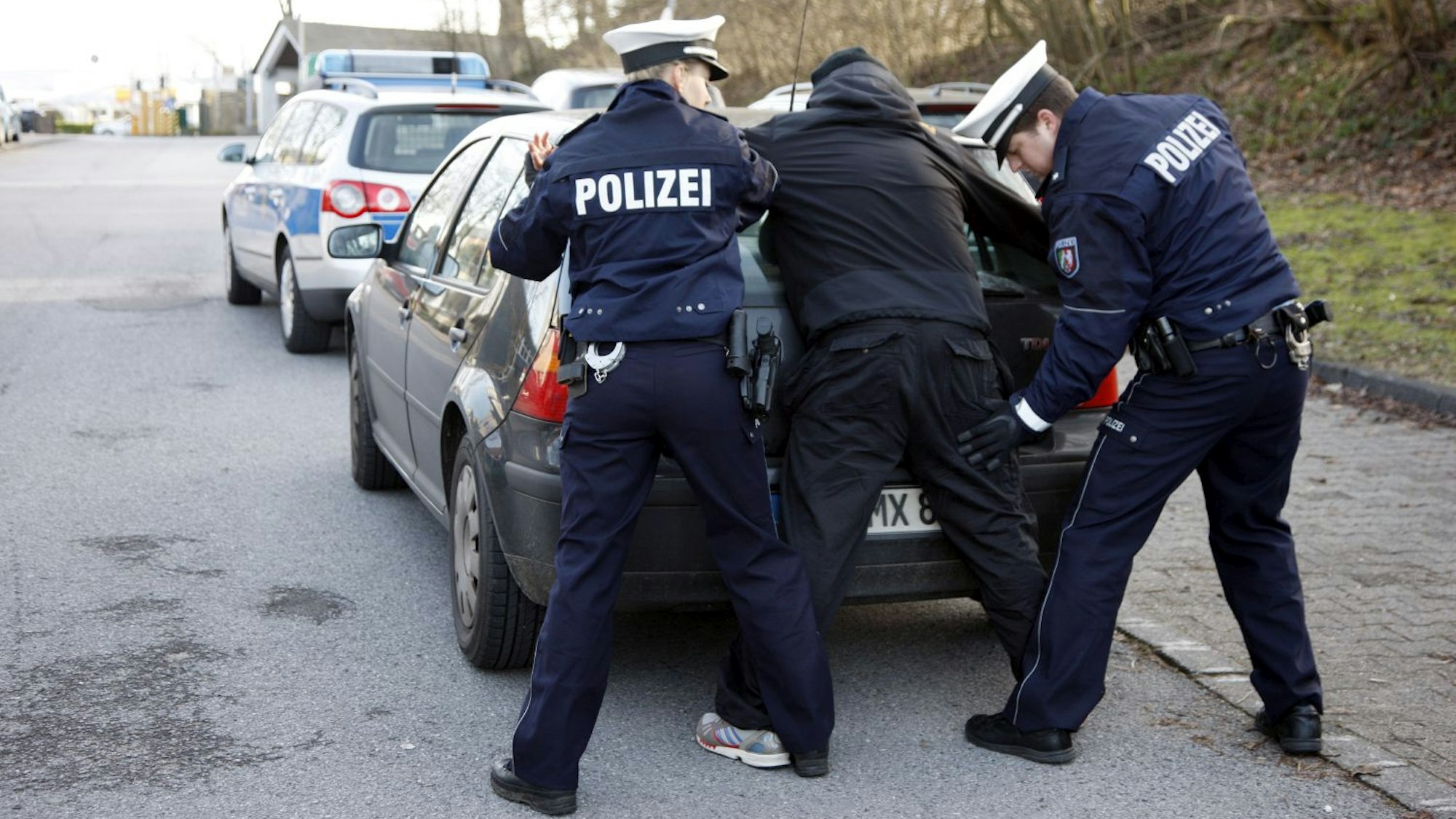 Polizisten kontrollieren eine Person am Heck ihres Pkw.