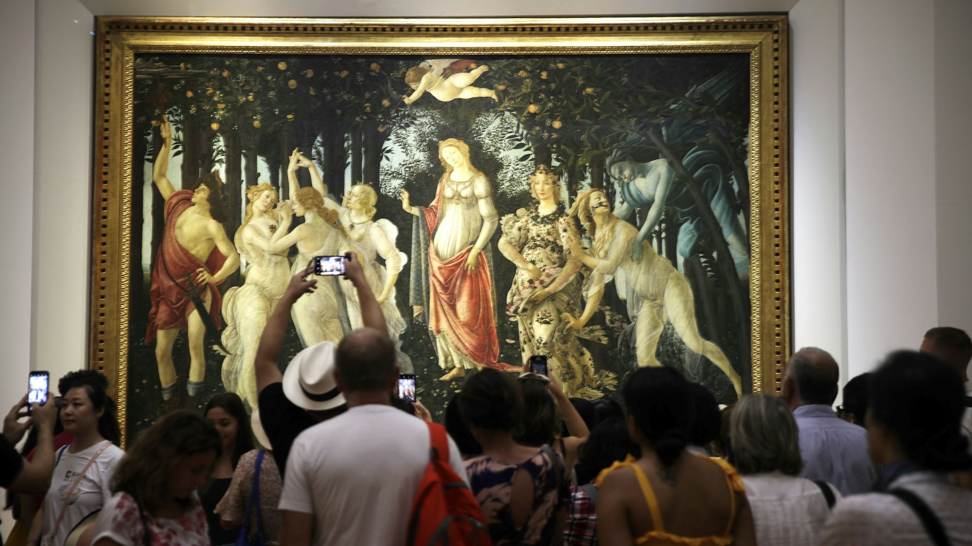 Mehrere Museumsbesucher stehen vor einem großen Kunstwerk, dem „Frühling” von Sandro Botticelli.