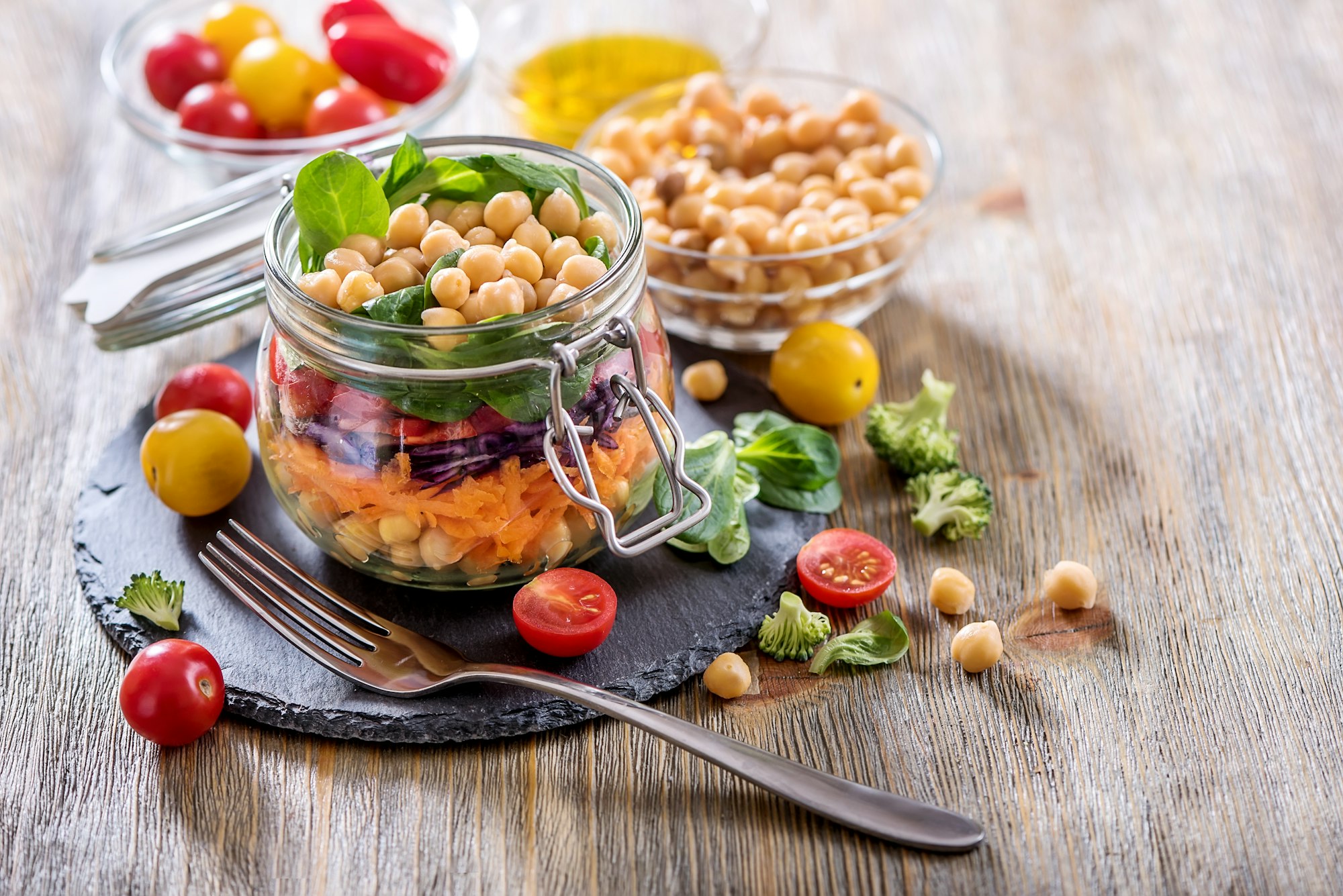 In einem Einmachglas ist ein Salat aus Kichererbsen, Möhre, Rotkraut, Paprika und Blattsalat angerichtet.