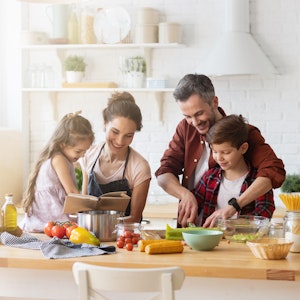 Eine Familie mit zwei Kindern steht in der Küche und kocht gemeinsam.