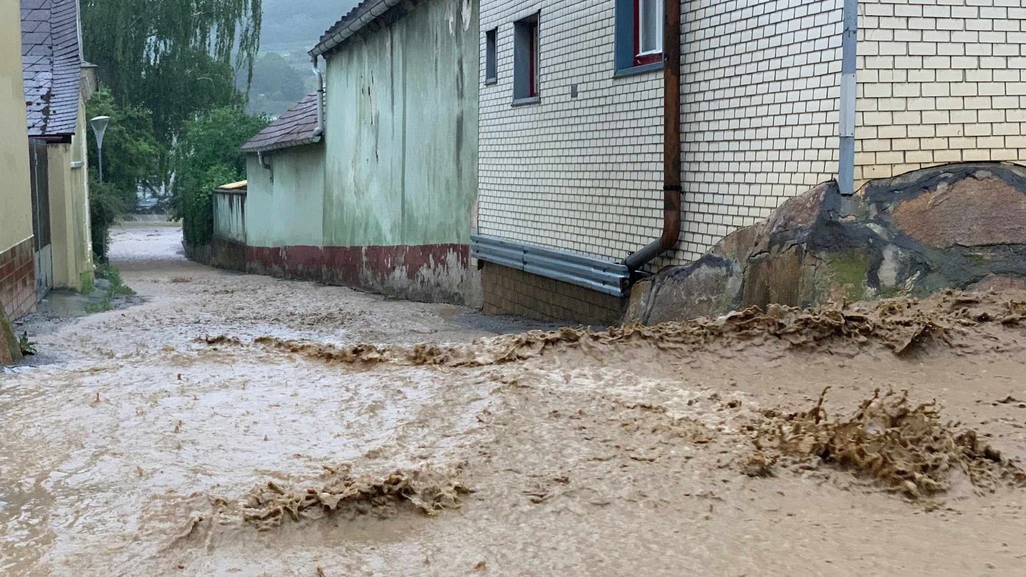 Wassermassen fluten eine Straße und fließen an Häusern vorbei.