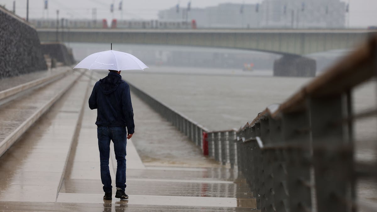 Ein Mann steht mit Regenschirm an der Freitreppe am Rheinufer.