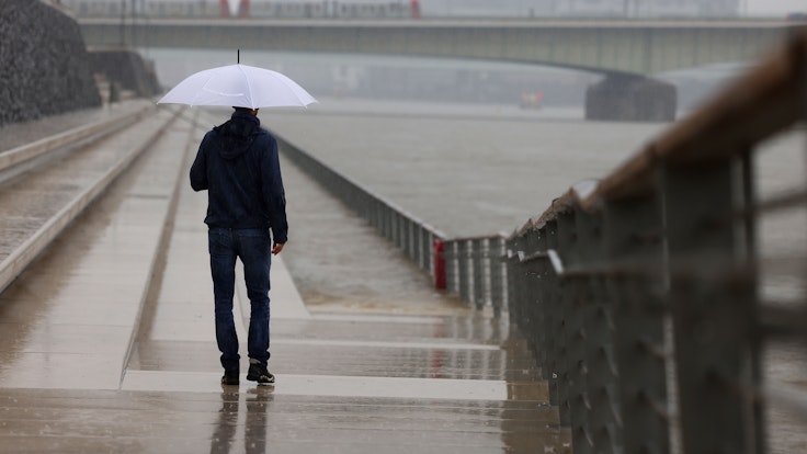 Ein Mann steht mit Regenschirm an der Freitreppe am Rheinufer. In Nordrhein-Westfalen werden in den nächsten Tagen Gewitter und viel Regen erwartet.