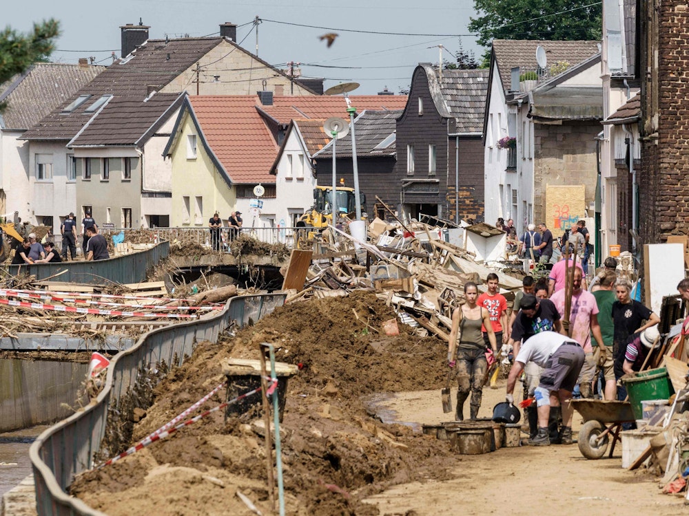 Helfer arbeiten auf einer von Matsch bedeckten Straße in Swisttal-Odendorf.