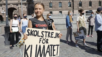 Greta Thunberg ist geimpft und hält ihr Schild mit der Aufschrift „Skolstrejk för Klimatet” in den Händen.