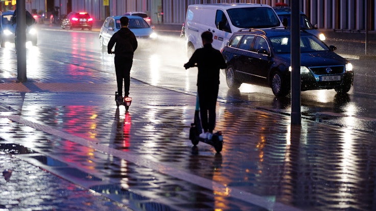 Junge Männer fahren bei Regen mit E-Scootern durch Köln.
