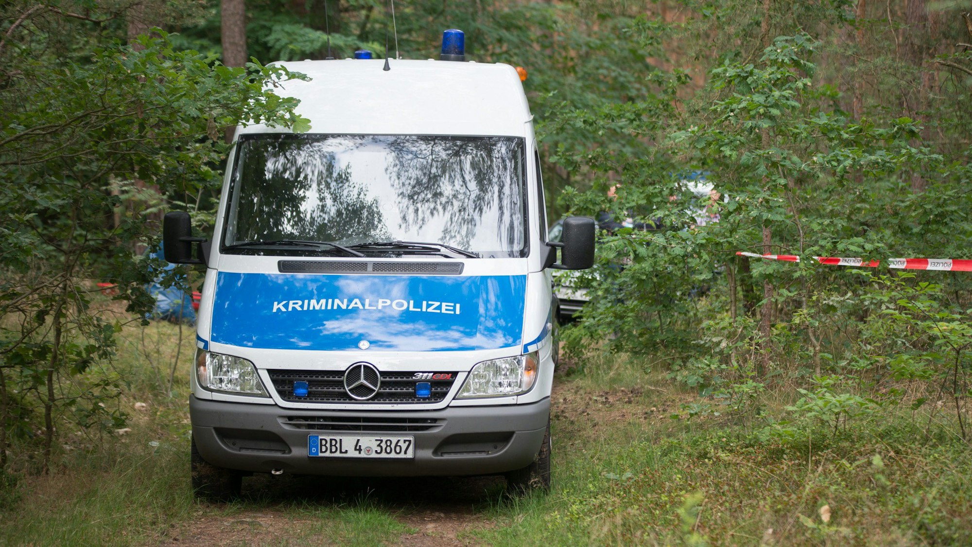 In einem Waldstück steht ein Einsatzfahrzeug der Brandenburger Kriminalpolizei.