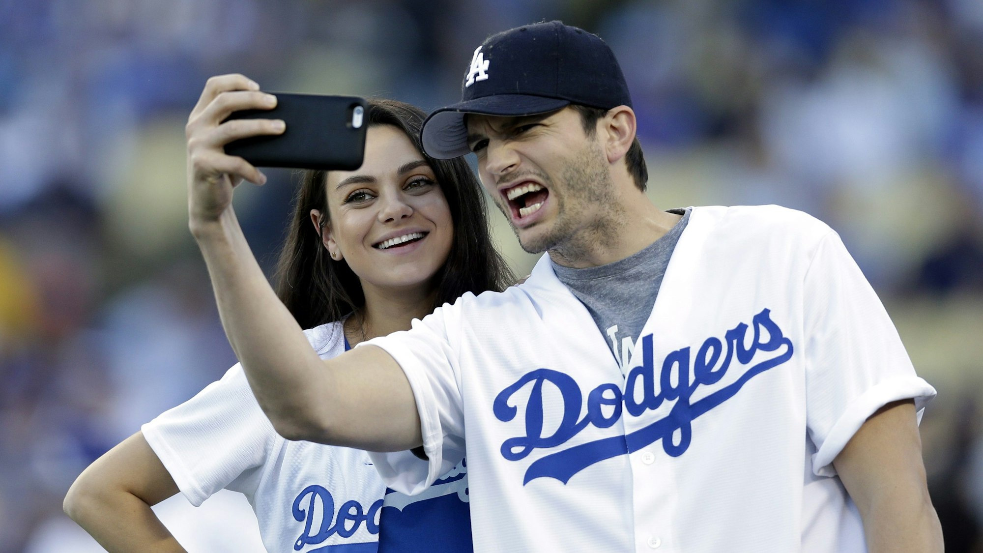 Ahston Kutcher macht ein Selfie von sich und Mila Kunis in Baseball-Outfits der Dodgers.