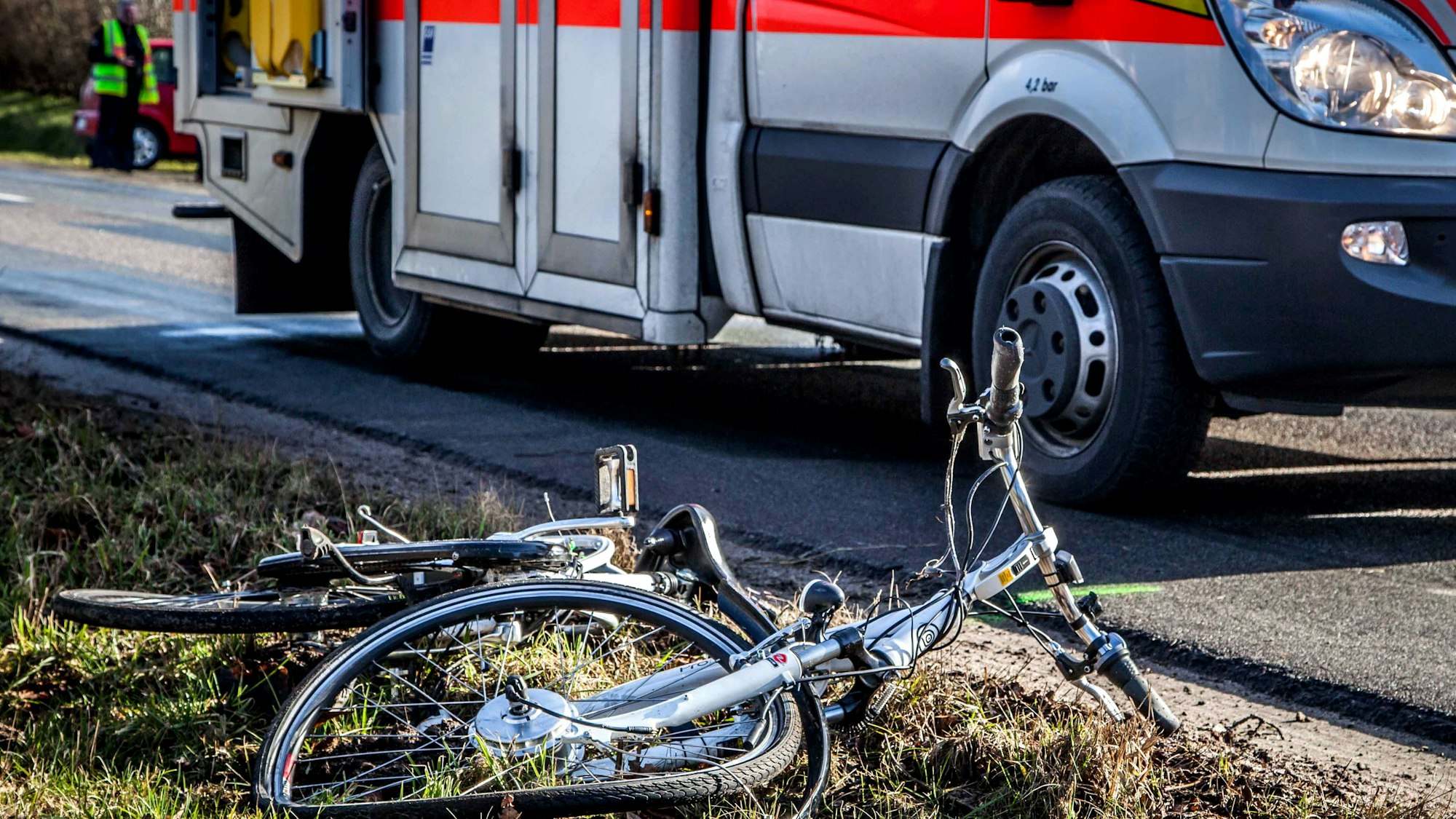 Ein zerstörtes Fahrrad liegt neben einer Straße, auf der ein Rettungswagen steht.