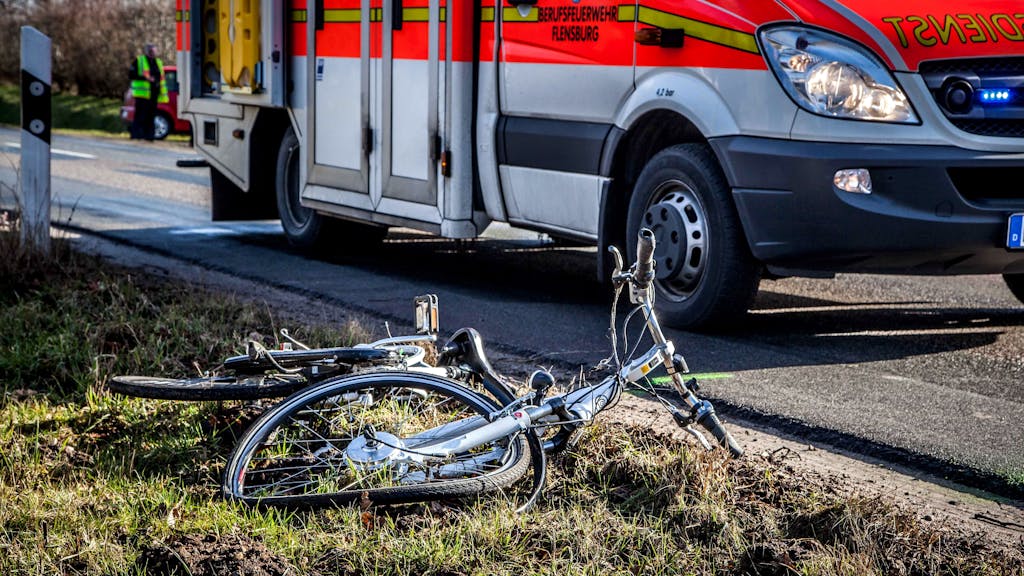 Ein zerstörtes Fahrrad liegt neben einer Straße, auf der ein Rettungswagen steht.