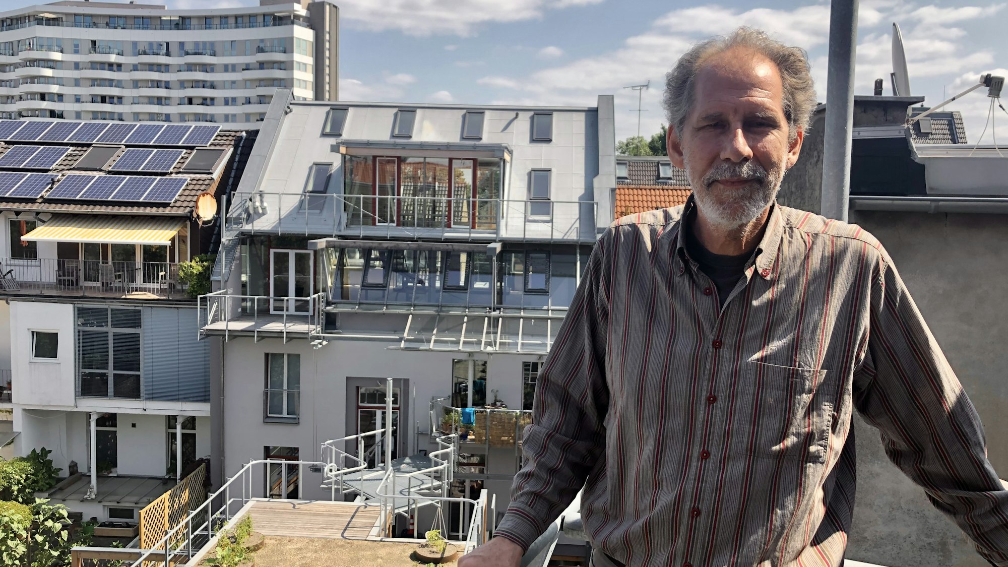 Architekt Gabor Schneider steht auf einem Balkon, der sich noch im Rohbau befindet. Im Hintergrund der Dachgarten und das Wohnhaus.
