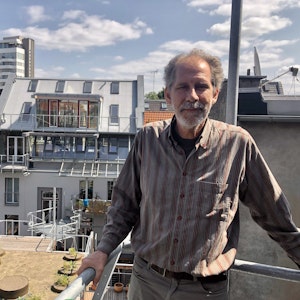 Architekt Gabor Schneider steht auf einem Balkon, der sich noch im Rohbau befindet. Im Hintergrund der Dachgarten und das Wohnhaus.