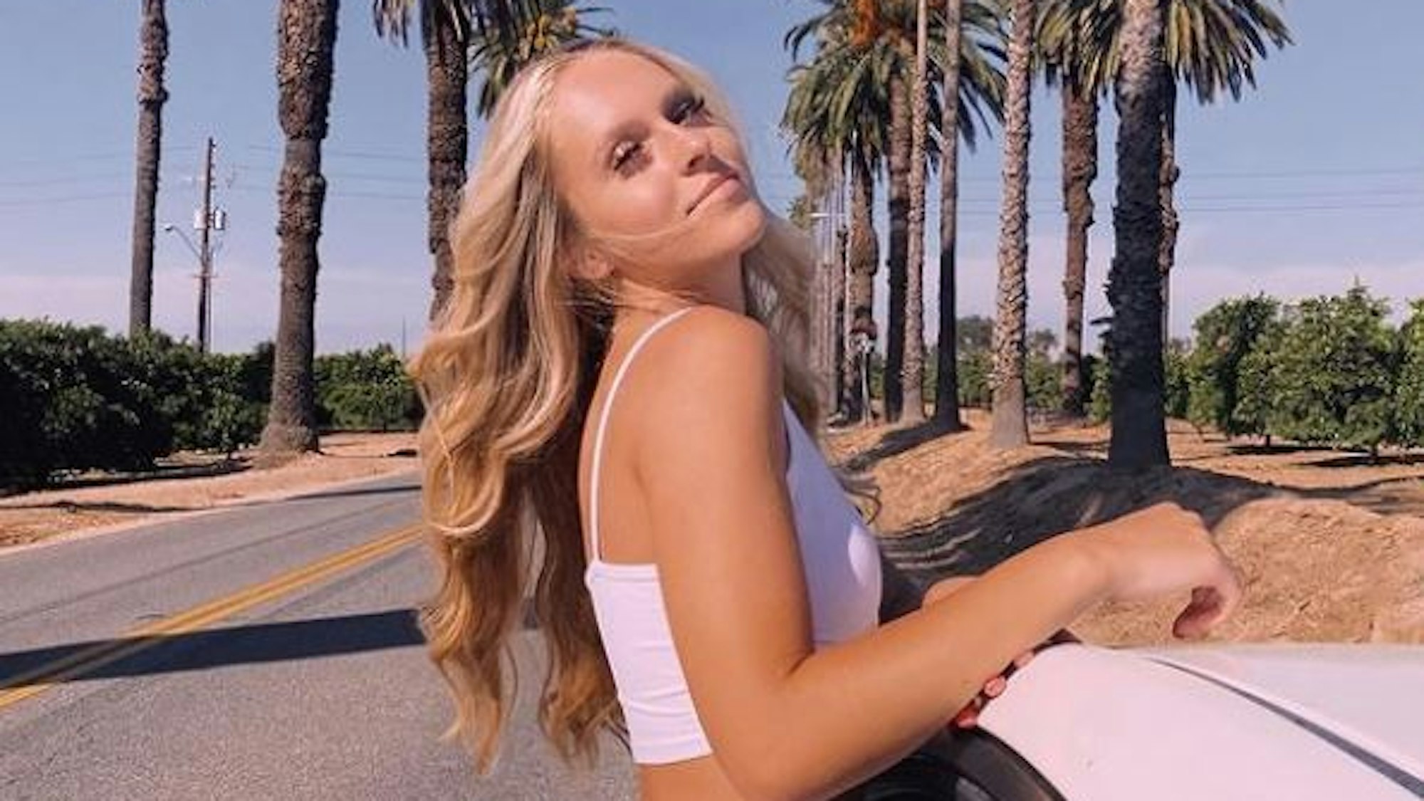 Die Teenagerin Rylee Goodrich sitzt im Fenster eines Autos, das auf einer mit Palmen gesäumten Straße steht.