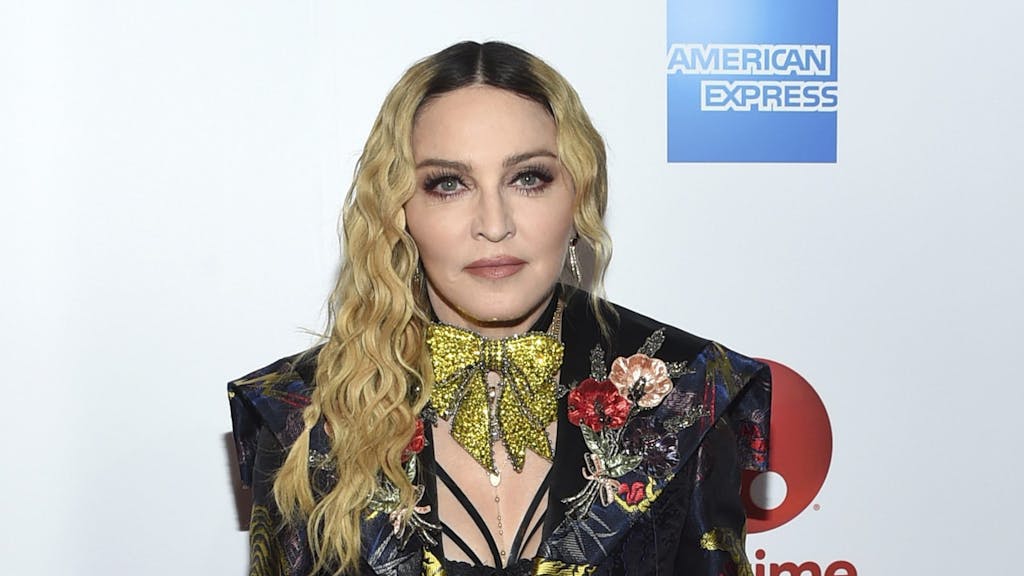 Madonna posiert im schwarzen Anzug mit auffälliger goldener Schleife um den Hals.