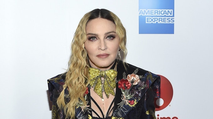 Madonna posiert im schwarzen Anzug mit auffälliger goldener Schleife um den Hals.